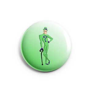 May include: A green button with a cartoon image of a man in a green suit with a question mark on the chest. The man is holding a cane and has a green hat on his head.