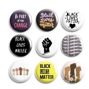 May include: Nine round black and white buttons with various designs and text. The buttons feature the phrase "Black Lives Matter" in different fonts and styles, along with a raised fist and a heart. One button says "Be Part of the Change".