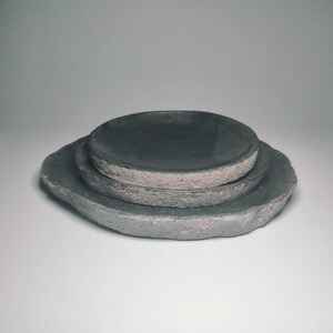 May include: Three grey ceramic plates stacked on top of each other. The plates have a rough, textured surface.