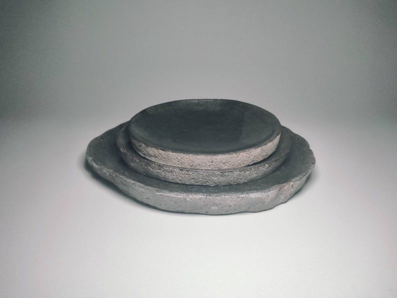 May include: Three grey ceramic plates stacked on top of each other. The plates have a rough, textured surface.