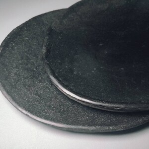 May include: Two black ceramic plates stacked on top of each other. The plates have a rough, textured surface.
