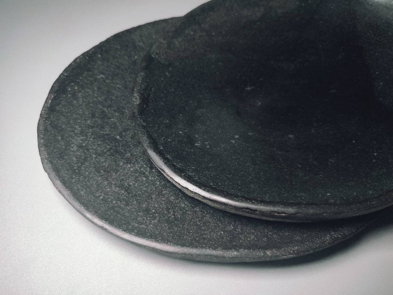 May include: Two black ceramic plates stacked on top of each other. The plates have a rough, textured surface.