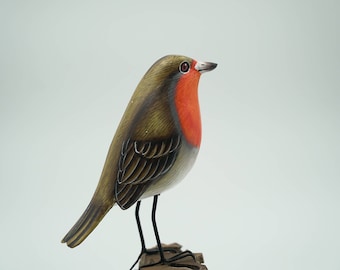 Pode incluir: Uma figura de pardal de madeira pintada à mão com penas castanhas, pretas e brancas, um peito vermelho e olhos pretos. O pardal está empoleirado num pequeno ramo de madeira.