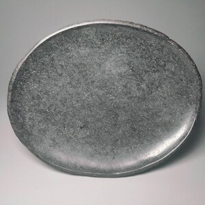 May include: A round, grey, stone plate with a slightly uneven edge.