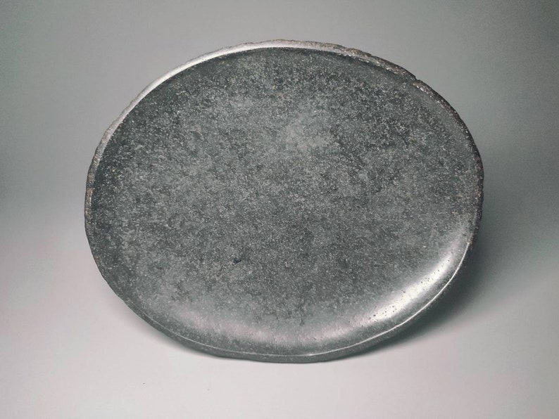 May include: A round, grey, stone plate with a slightly uneven edge.