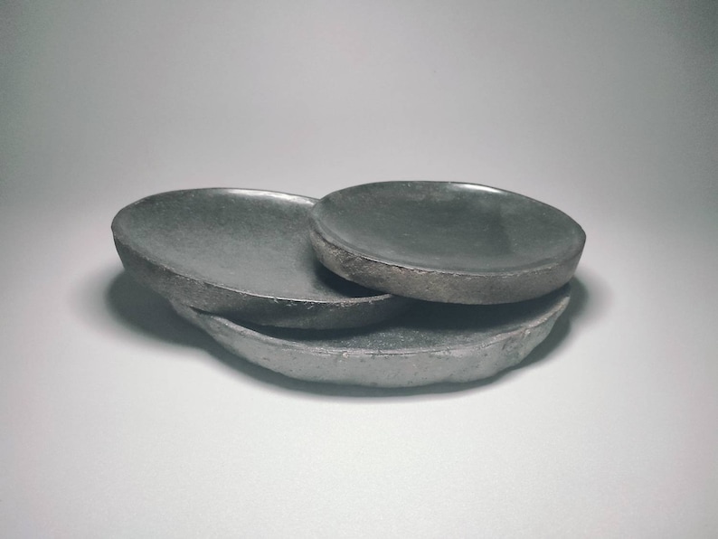 May include: Three grey ceramic dishes of varying sizes stacked on top of each other. The dishes have a rough, textured surface.