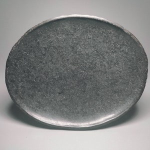 May include: A dark grey oval-shaped ceramic plate with a rough, textured surface.