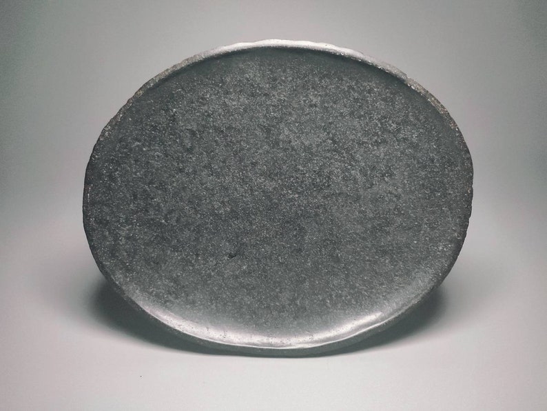 May include: A dark grey oval-shaped ceramic plate with a rough, textured surface.