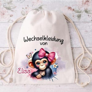 Könnte beinhalten: Ein weißer Kordelzugbeutel mit dem Text "Wechselkleidung von Elisa" und einer Cartoon-Illustration eines Affen mit einer rosa Schleife.