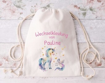 Könnte beinhalten: Ein weißer Kordelzugbeutel mit einem Einhorn- und Sternenmotiv. Der Beutel trägt die Aufschrift "Wechselkleidung von Pauline" in rosa Schrift.
