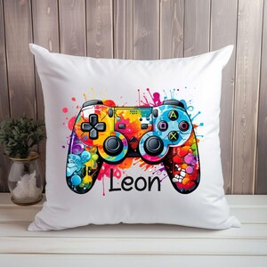 Könnte beinhalten: Ein weißes Kissen mit einer bunten Grafik eines Videospiel-Controllers und dem Namen Leon darunter.