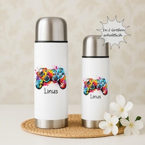 Könnte beinhalten: Zwei weiße isolierte Wasserflaschen mit silbernen Deckeln. Jede Flasche zeigt ein farbenfrohes Bild eines Videospiel-Controllers im Spritzstil und den Namen "Linus" in Schwarz. Die Flaschen stehen auf einer gewebten Matte mit weißen Blumen.
