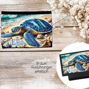 Könnte beinhalten: Schwarzes Portemonnaie mit einem blauen Meeresschildkröten-Motiv am Strand, umgeben von Muscheln und dem Namen "Ella". Das Portemonnaie hat einen schwarzen Rand.