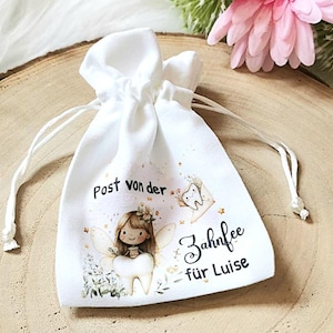 May include: A white fabric bag with a drawstring closure. The bag has a printed design of a tooth fairy with a tooth, flowers, and stars. The text on the bag reads "Post von der Zahnfee f&uuml;r Luise".