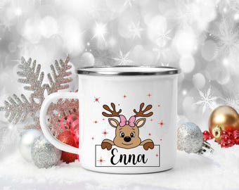 Könnte beinhalten: Weiße Email Tasse mit einem rotnasigen Rentier mit einer rosa Schleife, das über den Rand der Tasse schaut. Die Tasse hat einen weißen Hintergrund mit roten Sternen und den Namen "Enna" auf der Vorderseite.