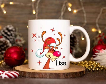Könnte beinhalten: Weiße Keramiktasse mit einem Cartoon-Rentier, das einen Weihnachtsmann-Hut trägt, und dem Namen "Lisa" auf der Vorderseite. Die Tasse ist von Weihnachtsdekoration umgeben.