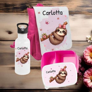 Könnte beinhalten: Ein rosa Rucksack, eine Wasserflasche und ein Lunchbox-Set. Jeder Artikel trägt den Namen "Carlotta" und ein Cartoon-Faultier mit einer rosa Schleife. Das Faultier hängt an einem Ast mit Blumen. Die Wasserflasche hat einen schwarzen Deckel.