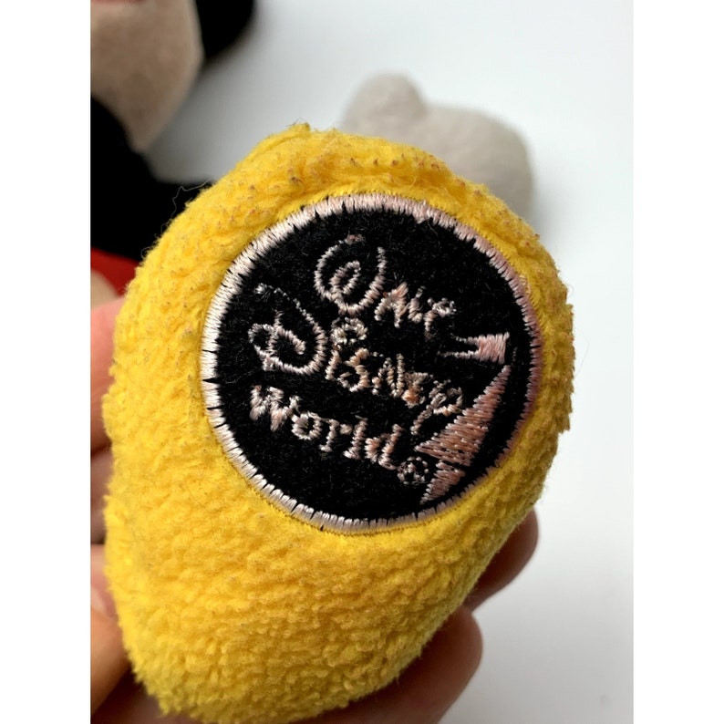 May include: Yellow plush toy with a black and white embroidered patch that reads "Walt Disney World".