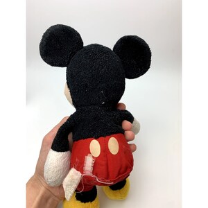 May include: A black and red plush Mickey Mouse toy with large ears. The toy is wearing red shorts with two yellow circles. The toy is in good condition, but there is some wear and tear on the fabric.