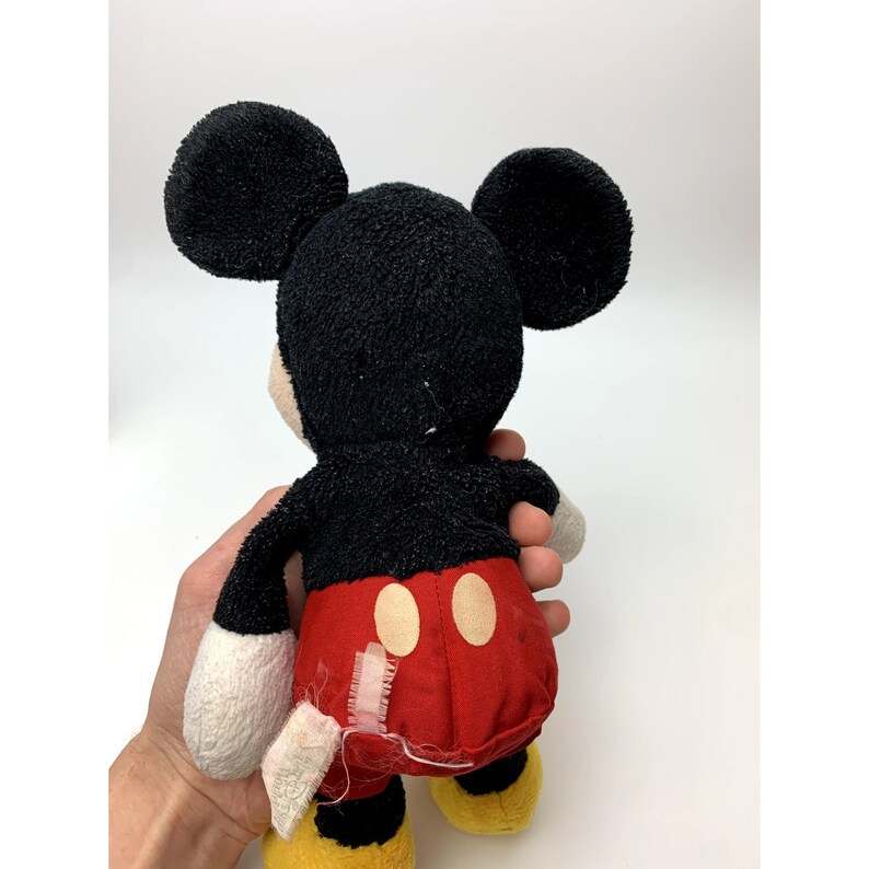 May include: A black and red plush Mickey Mouse toy with large ears. The toy is wearing red shorts with two yellow circles. The toy is in good condition, but there is some wear and tear on the fabric.
