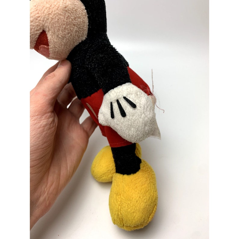 May include: A vintage plush Mickey Mouse toy with black fur, red shorts, white gloves, and yellow shoes. The toy is slightly worn and has a few loose threads.