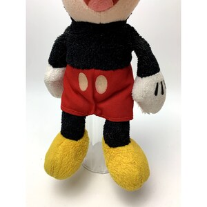 May include: A plush Mickey Mouse toy with black fur, red shorts with two yellow buttons, and yellow shoes.