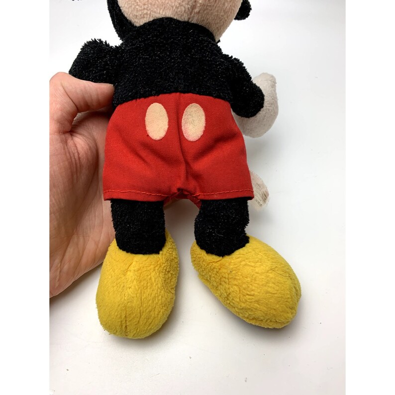 May include: A plush Mickey Mouse toy with black fur, red shorts with two yellow buttons, and yellow shoes.