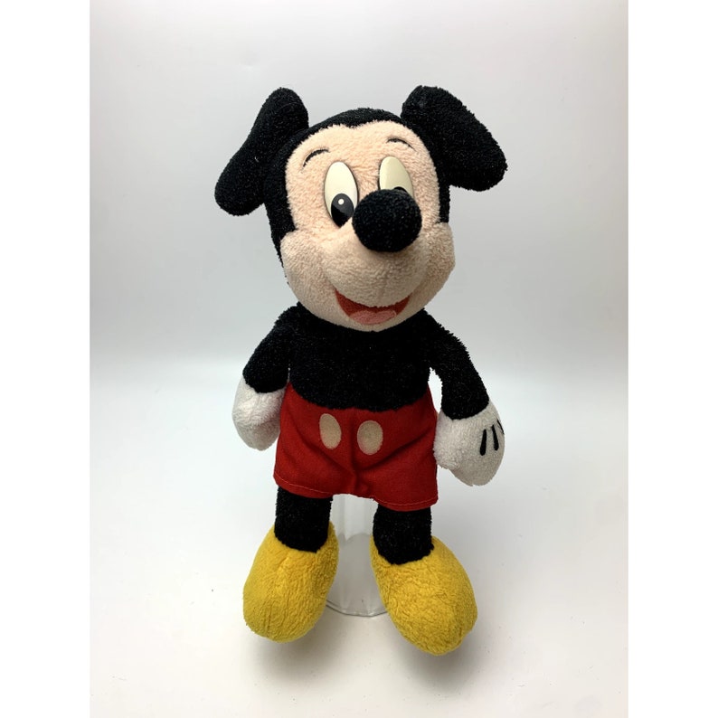 May include: A plush black and red Mickey Mouse toy with yellow shoes. The toy has a smiling face with black eyes and a black nose.