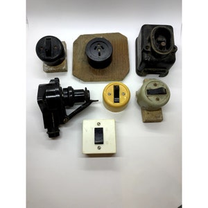Puede incluir: Surtido de interruptores y enchufes eléctricos vintage en plástico negro y blanco. Los interruptores tienen una variedad de formas y tamaños, incluyendo redondos, cuadrados y rectangulares. Algunos de los interruptores tienen un solo interruptor, mientras que otros tienen interruptores múltiples. Los enchufes son todos de tamaño estándar y tienen una variedad de configuraciones.