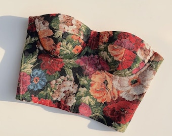 May include: A strapless floral print bustier top with a black background and colorful flowers. The bustier has a boned structure and a sweetheart neckline.