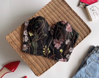 May include: A black strapless top with floral embroidery. The embroidery features pink, green, and white flowers on a black mesh fabric.
