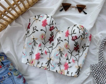 May include: White strapless top with a floral embroidery design. The embroidery features pink, blue, and red flowers on a white background.