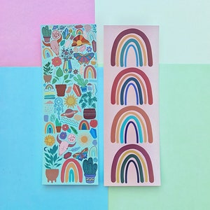 Pode incluir: Dois autocolantes retangulares. Um é verde-azulado claro com ilustrações coloridas de plantas, cristais e uma borboleta. O outro é rosa claro com quatro desenhos de arco-íris em tons de castanho, azul e amarelo. O fundo é uma mistura de rosa, azul e verde.