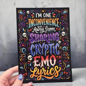 May include: A rectangular black card featuring colorful, stylized typography that reads: I'M ONE INCONVENIENCE AWAY FROM SHARING CRYPTIC EMO LYRICS. The design is surrounded by decorative swirls, small skulls, broken hearts, and musical notes in vibrant hues.