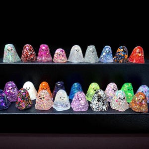 Collection of small glittery resin ghost figurines in different colours, displayed on black steps for a lucky dip random selection