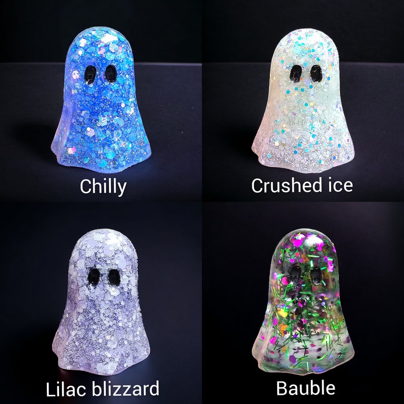May include: Four glittery ghost figurines in blue, white, lavender, and green. Each ghost has black oval eyes and a different glitter color scheme. The text labels each ghost: "Chilly", "Crushed ice", "Lilac blizzard", and "Bauble".