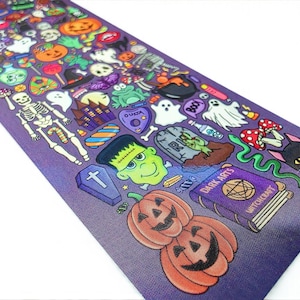 Puede incluir: Un camino de mesa decorativo con tem&aacute;tica de Halloween de color p&uacute;rpura con varias ilustraciones de dibujos animados. El dise&ntilde;o incluye calabazas, fantasmas, un esqueleto, Frankenstein, una tabla Ouija y un libro con la leyenda "Dark Arts Witchcraft".