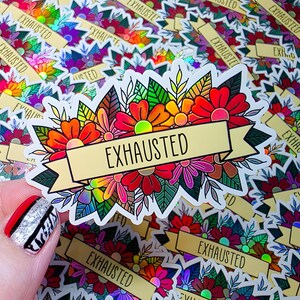 May include: A sticker with a floral design in red, orange, pink, and yellow, with green leaves. The word "EXHAUSTED" is written on a gold banner across the flowers. Other stickers with the same design are in the background.