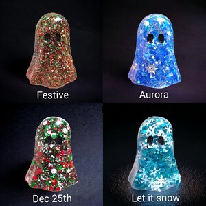 May include: Four resin ghost figurines in different colors. The first is brown with glitter and the word "Festive". The second is blue with stars and the word "Aurora". The third is red and green with the words "Dec 25th". The fourth is blue with snowflakes and the words "Let it snow".