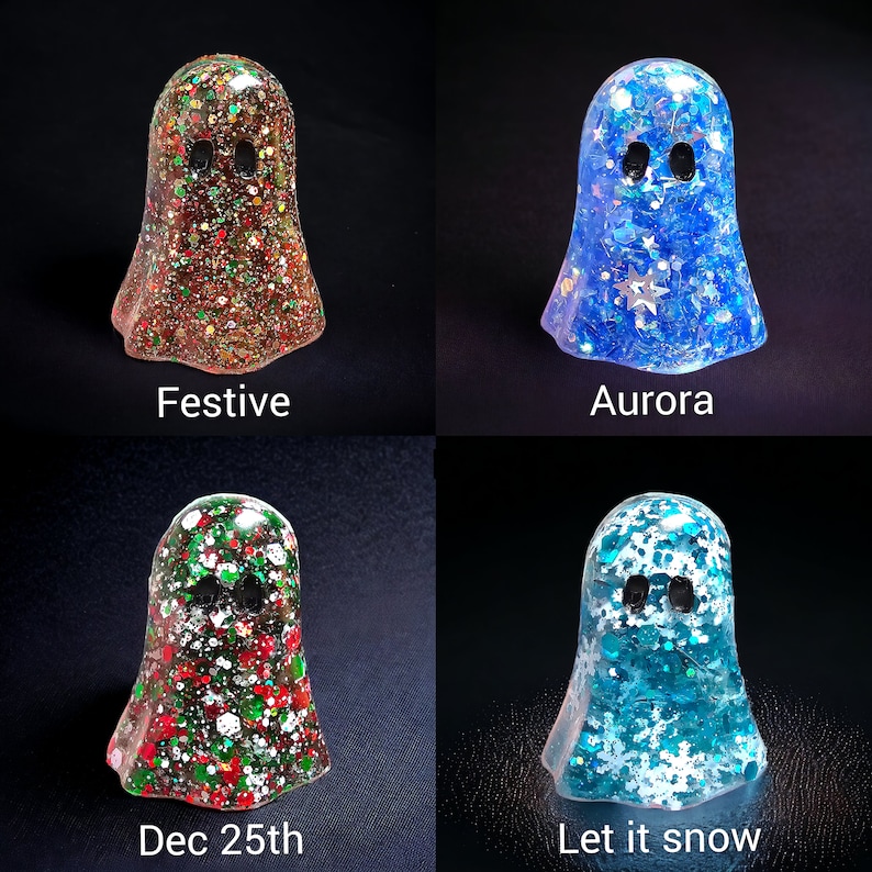 May include: Four resin ghost figurines in different colors. The first is brown with glitter and the word "Festive". The second is blue with stars and the word "Aurora". The third is red and green with the words "Dec 25th". The fourth is blue with snowflakes and the words "Let it snow".