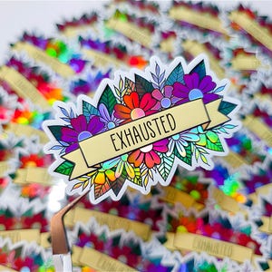 May include: A holographic sticker featuring a floral design with the word "EXHAUSTED" on a banner. The sticker has a colorful array of flowers in shades of red, orange, purple, and white, with green leaves. The background is filled with similar stickers.