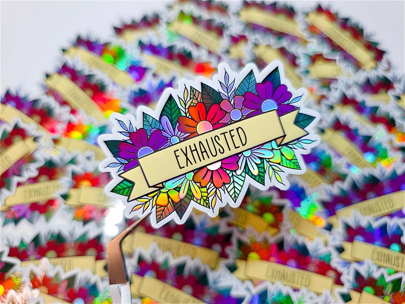 May include: A holographic sticker featuring a floral design with the word "EXHAUSTED" on a banner. The sticker has a colorful array of flowers in shades of red, orange, purple, and white, with green leaves. The background is filled with similar stickers.