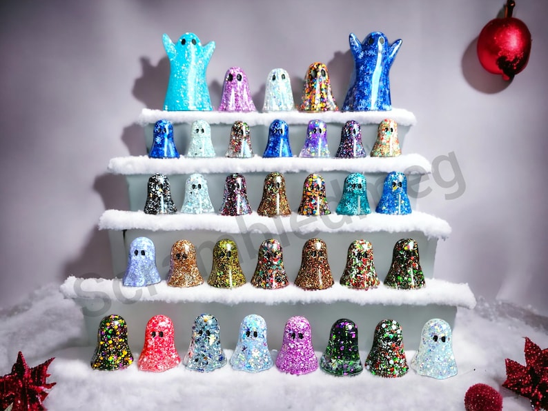 May include: A display of glittery ghost figurines in various colors, arranged on tiered platforms with faux snow. The ghosts have different patterns and colors, including blue, purple, gold, and red. A festive, decorative theme.