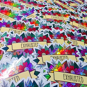 May include: A collection of stickers with a floral design and the word "EXHAUSTED" on a banner. The stickers feature a variety of colors, including red, purple, green, and yellow. The floral design is detailed and intricate, with a holographic effect.