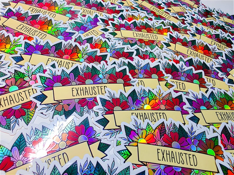 May include: A collection of stickers with a floral design and the word "EXHAUSTED" on a banner. The stickers feature a variety of colors, including red, purple, green, and yellow. The floral design is detailed and intricate, with a holographic effect.
