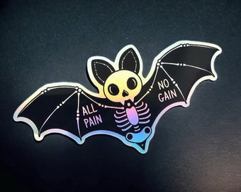 May include: A holographic sticker in the shape of a bat with a skeleton design. The bat has the words "ALL PAIN" and "NO GAIN" on its wings. The bat's body has a gradient of colors, including yellow, pink, and blue.