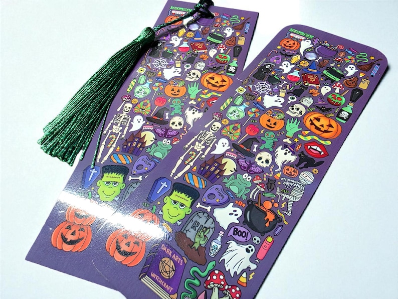 Puede incluir: Dos marcap&aacute;ginas morados con tem&aacute;tica de Halloween con borlas verdes. Los marcap&aacute;ginas est&aacute;n cubiertos de ilustraciones coloridas de calabazas, fantasmas, esqueletos y otros elementos espeluznantes. El texto "DARK ARTS" y "WITCHCRAFT" es visible en un libro.