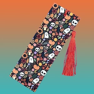 Pode incluir: Um marcador de livros decorativo com tema de Halloween. O marcador de livros apresenta um fundo preto com um padrão de abóboras, fantasmas, caveiras, flores e folhas. Uma borla vermelha está presa. Aproximadamente 20 cm de comprimento.
