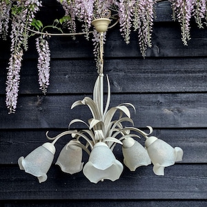 May include: A white metal chandelier with six frosted glass bell-shaped shades. The chandelier has a floral design and is hanging from a chain.