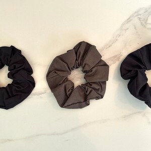 May include: Three fabric scrunchies in black, dark gray, and light gray. The scrunchies are made of soft, stretchy fabric and are perfect for holding hair in place.